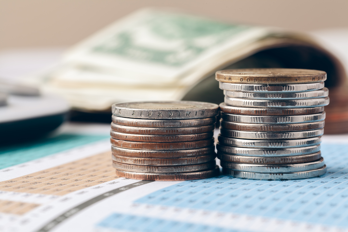 Monedas apiladas sobre un gráfico financiero con billetes al fondo.