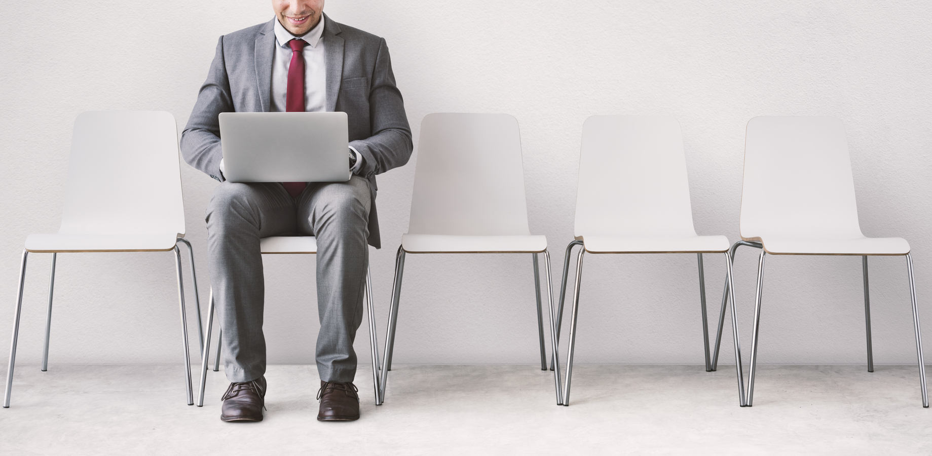 Hombre de negocios con traje utilizando una laptop mientras espera sentado.